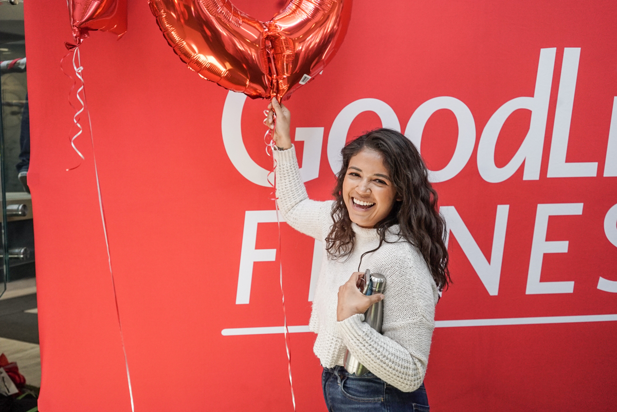A person holding balloons and smiling in front of a GoodLife Fitness sign