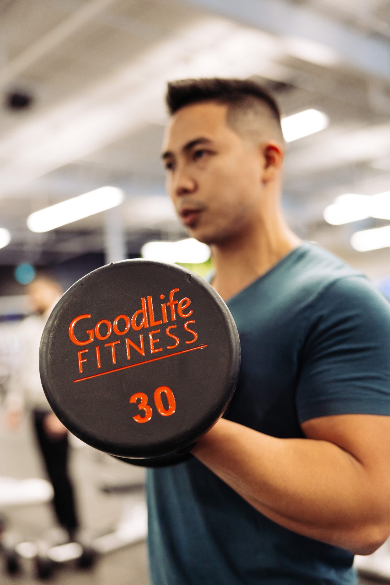 A man performing a bicep curl with a 30lb barbell in a GoodLife Fitness Club